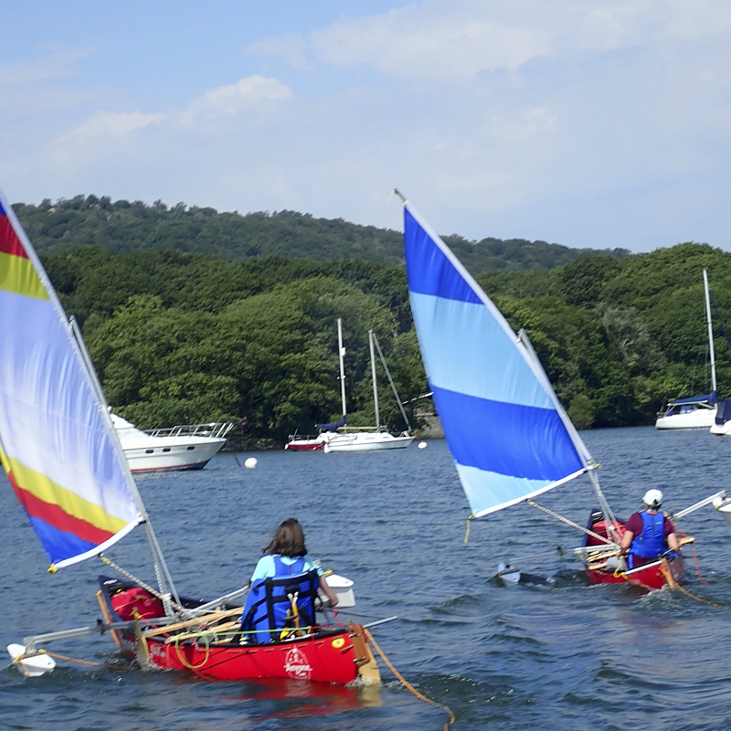 Person in blue boyancy aid is in a leaning sailing canoe