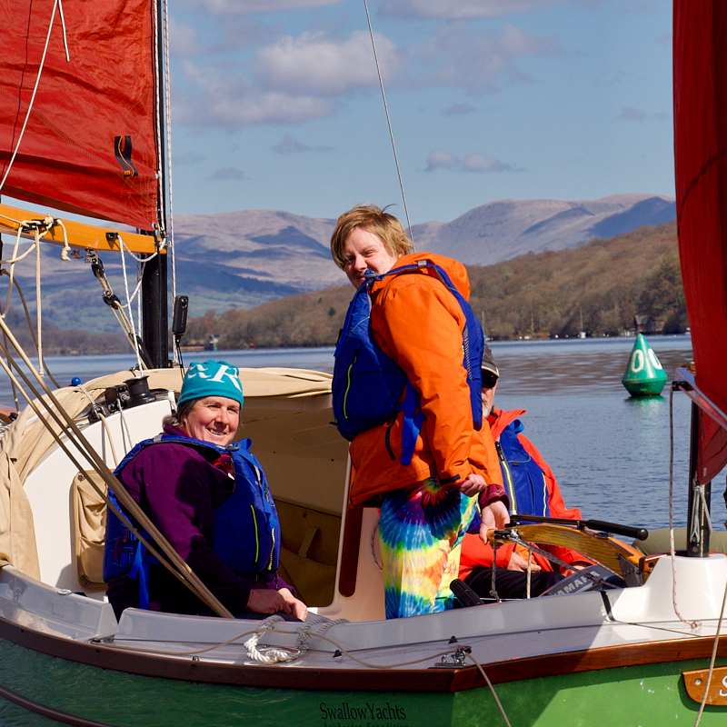 Lady in orange and bright leggings stands in a sailboat with red sails
